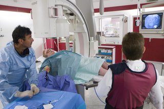 En patient, der ligger på et røntgenbord ved siden af en læge, der ser på et billede af patientens blodkar på en skærm